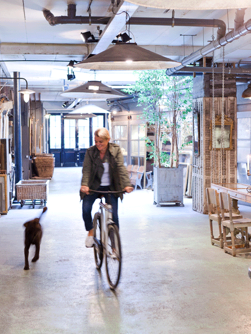 Anouk Beerents op fiets in atelier met hond en grote spiegels aan muur